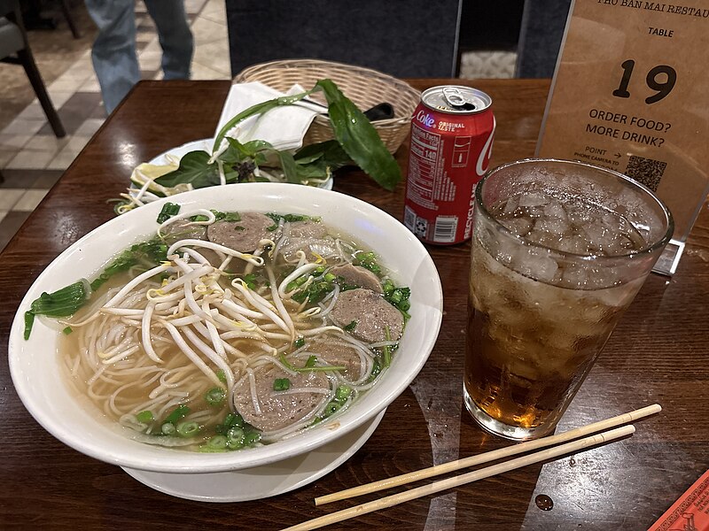 A bowl of phở topped with meatballs and herbs