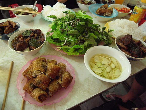 A bún chả table in Hanoi: grilled pork in broth, plain noodle cakes, a plate of herbs and pickled green papaya